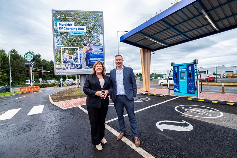 Cabinet Secretary for Transport, Fiona Hyslop and Lead Director, EV at SSE Energy Solutions, Simon Cowling pose in front of an EV charging bay at the Myrekirk Roundabout in Dundee.